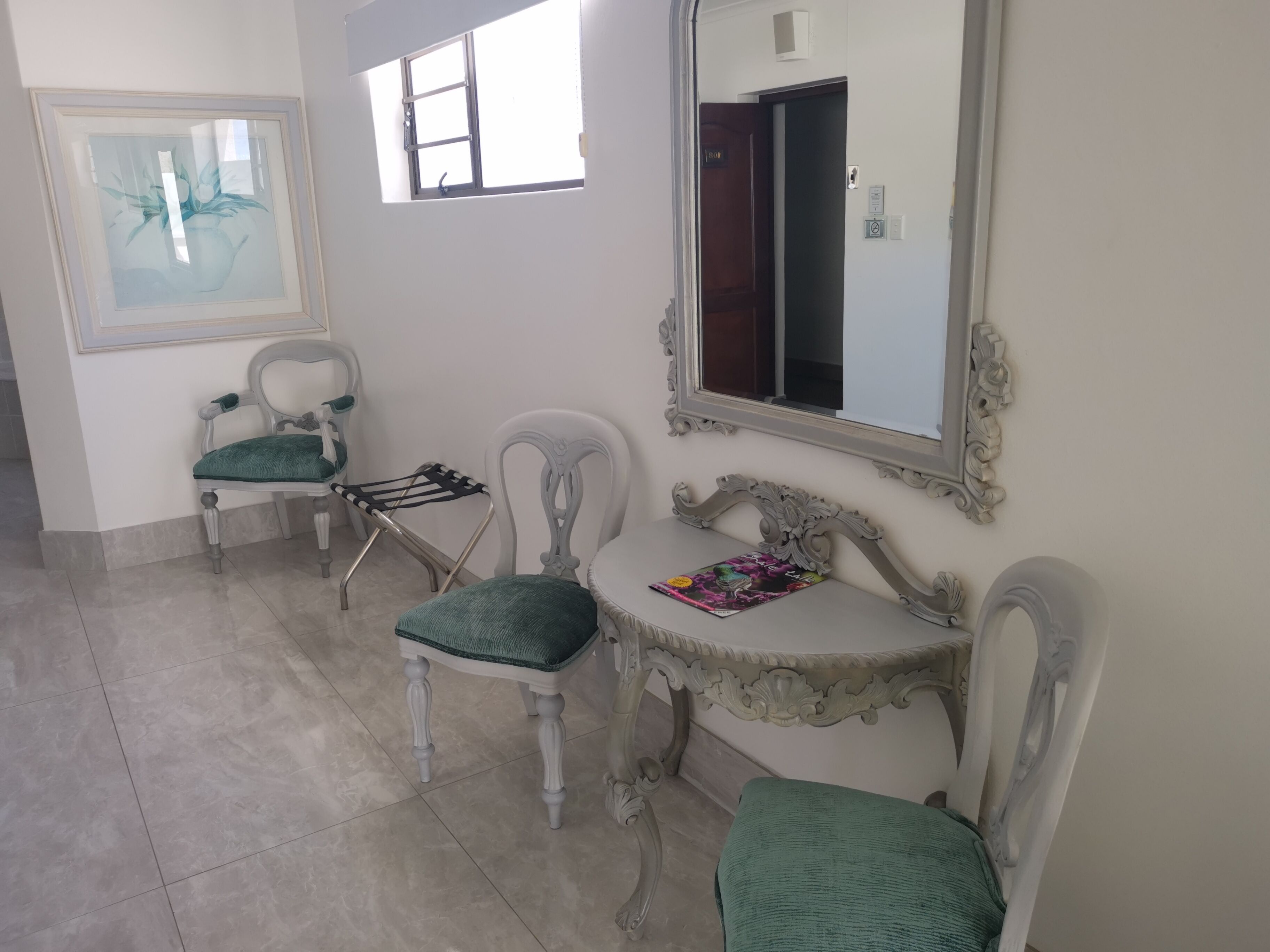 A room with two chairs, a small table, a mirror, and a window.