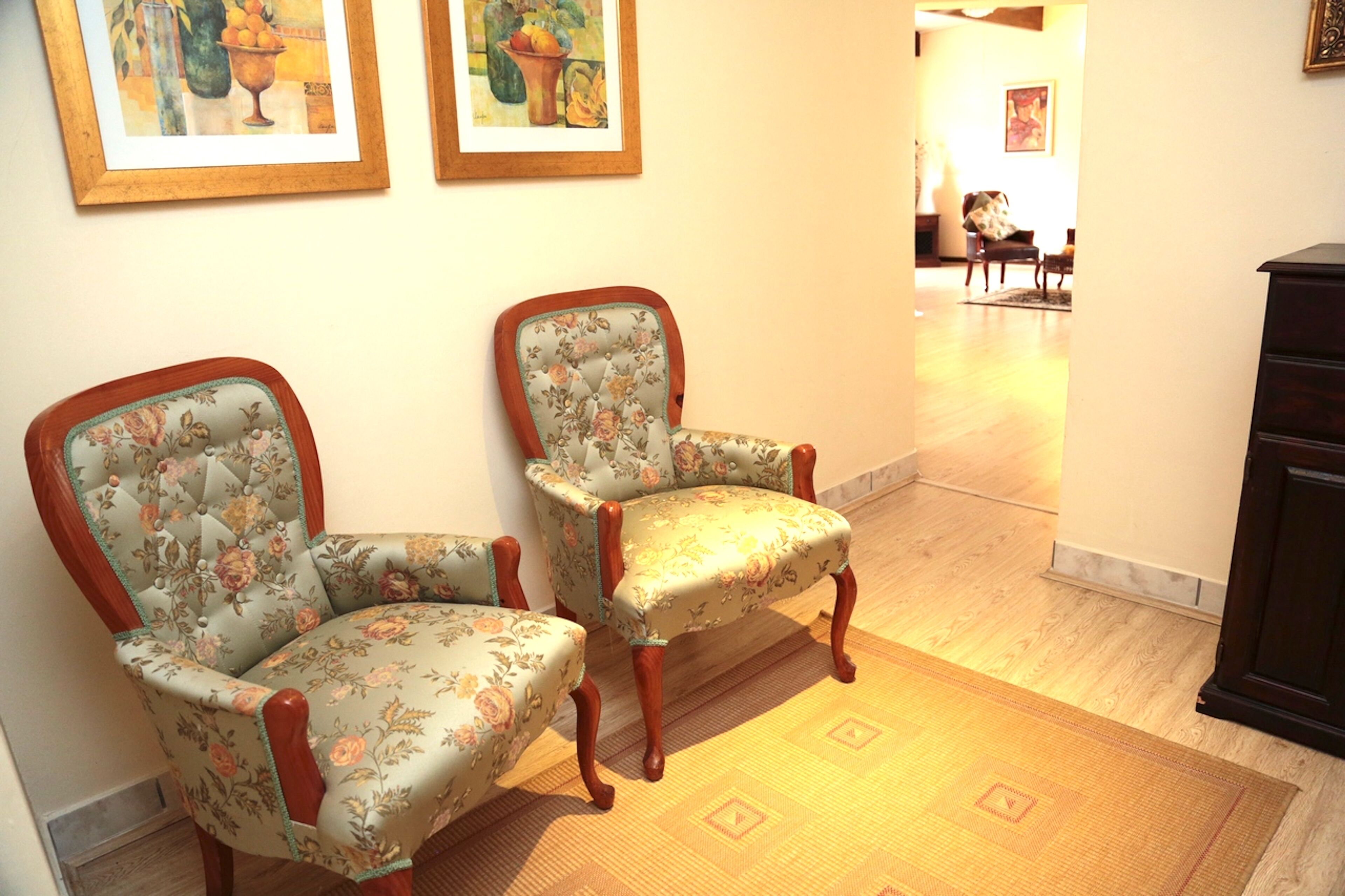 Two upholstered chairs with floral patterns, a wooden floor, and a dark-colored cabinet.