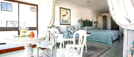 A bedroom with a bed, a chair, a table, and a painting on the wall.