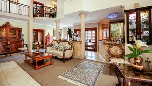 A spacious, elegantly furnished living room with a high ceiling, ornate furniture, and a grand staircase. - Misty Waves Boutique Hotel (Hermanus)