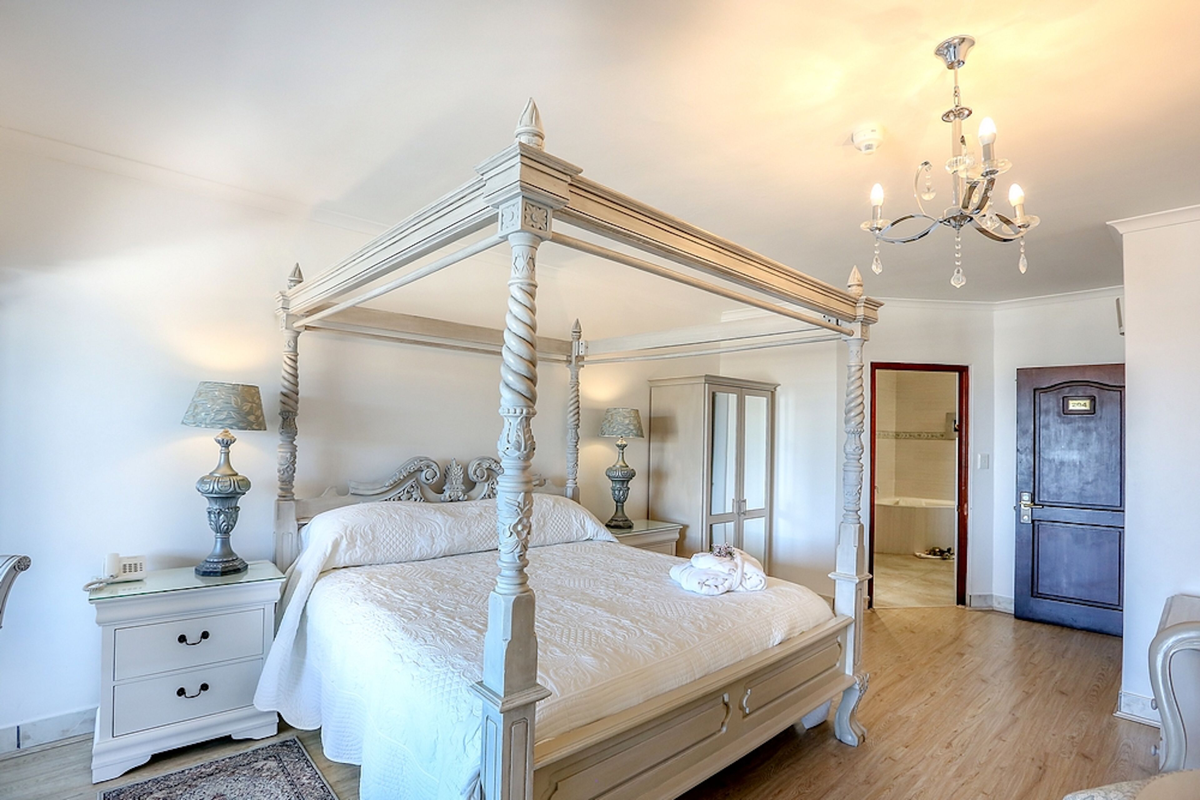 A four-poster bed with a mirror, bedside tables, and a chandelier.