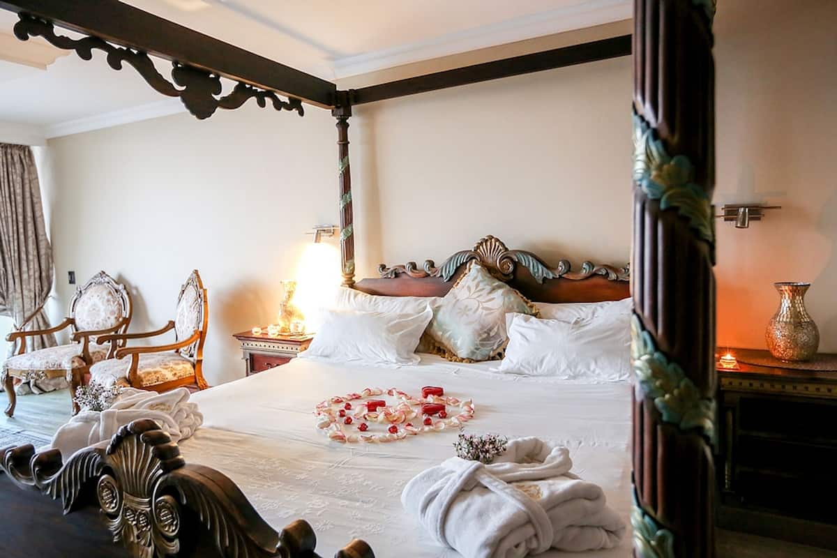 Una cama con dosel con sábanas blancas, una mesita de noche con lámpara y una silla con cojín floral.
