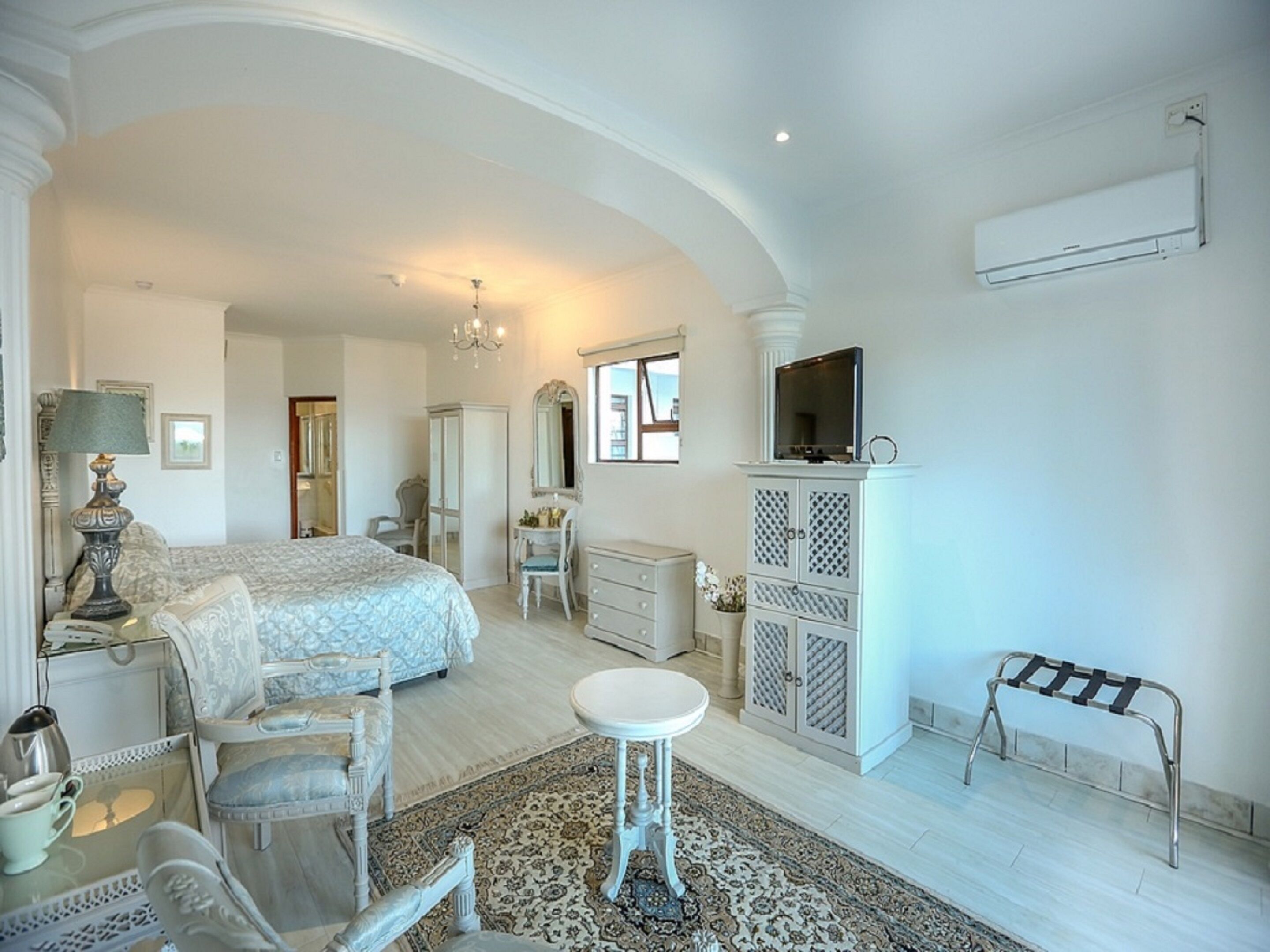 Une chambre spacieuse avec un grand lit, un coin salon avec une table et des chaises, une armoire et un téléviseur.