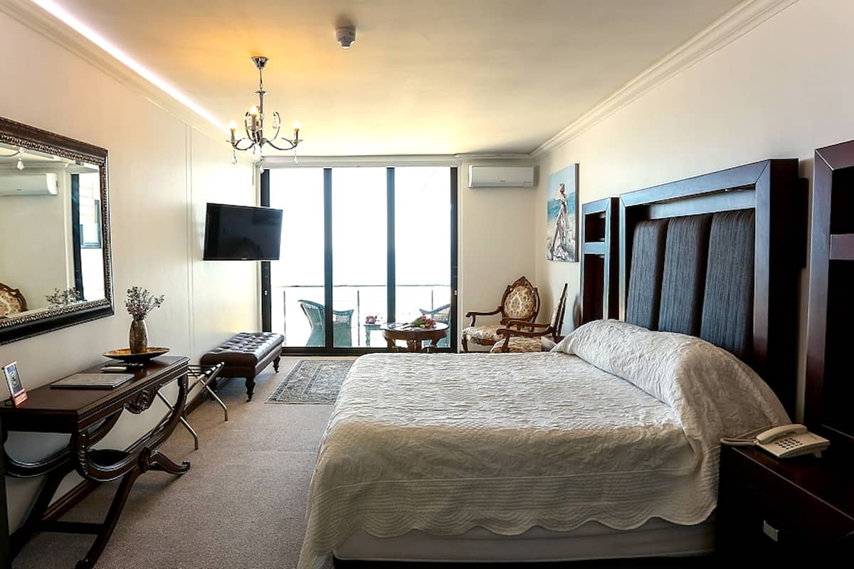 Une chambre d’hôtel avec un grand lit, un bureau avec un ordinateur, une chaise, une télévision et un balcon avec vue.