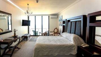 A hotel room with a large bed, a desk with a computer, a chair, a TV, and a balcony with a view.