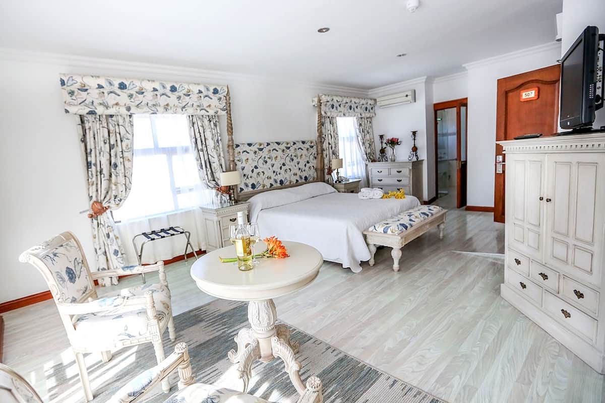Une chambre avec un grand lit, une table de chevet avec une lampe, une chaise, une petite table avec des fleurs et une armoire.