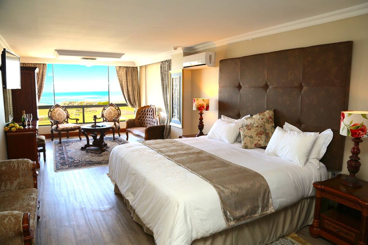 Une chambre d’hôtel avec un grand lit, un coin salon avec une table et des chaises, et une vue sur l’océan.