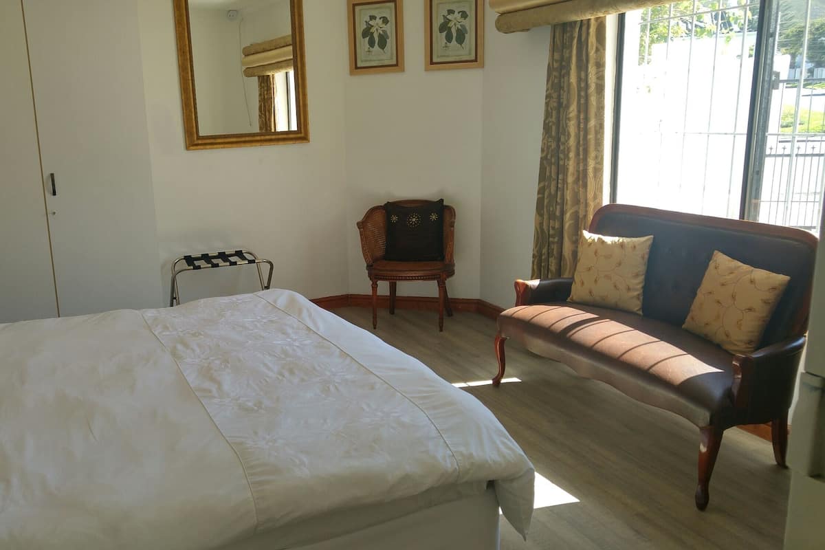 Un dormitorio con cama, una silla, un sofá, un espejo y una ventana con cortinas.