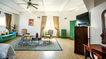 A living room with a ceiling fan, a green sofa, two armchairs, a coffee table, a TV, and a green cabinet.