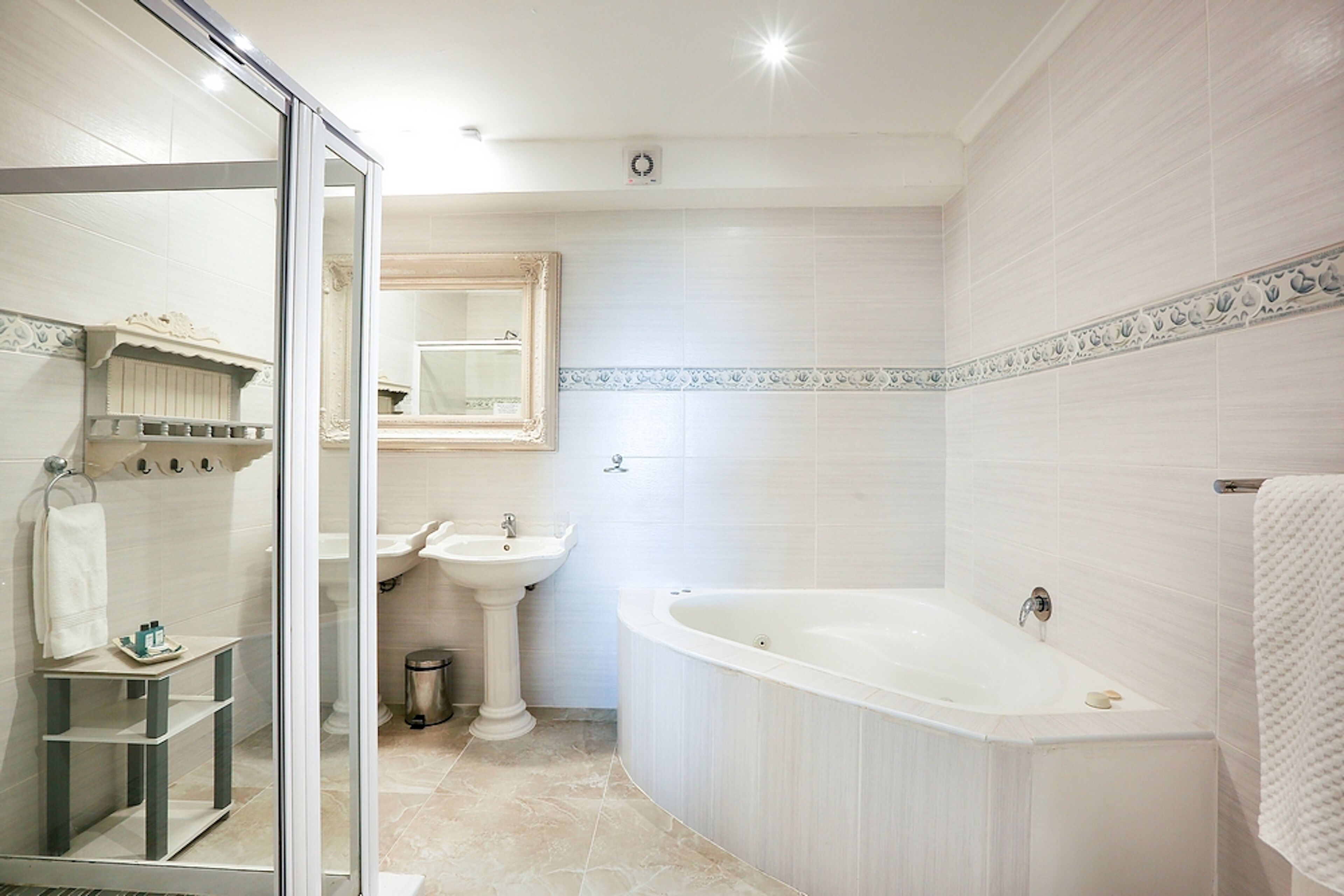 A modern bathroom with a glass shower enclosure, a pedestal sink, a freestanding bathtub, and a vanity with a mirror.