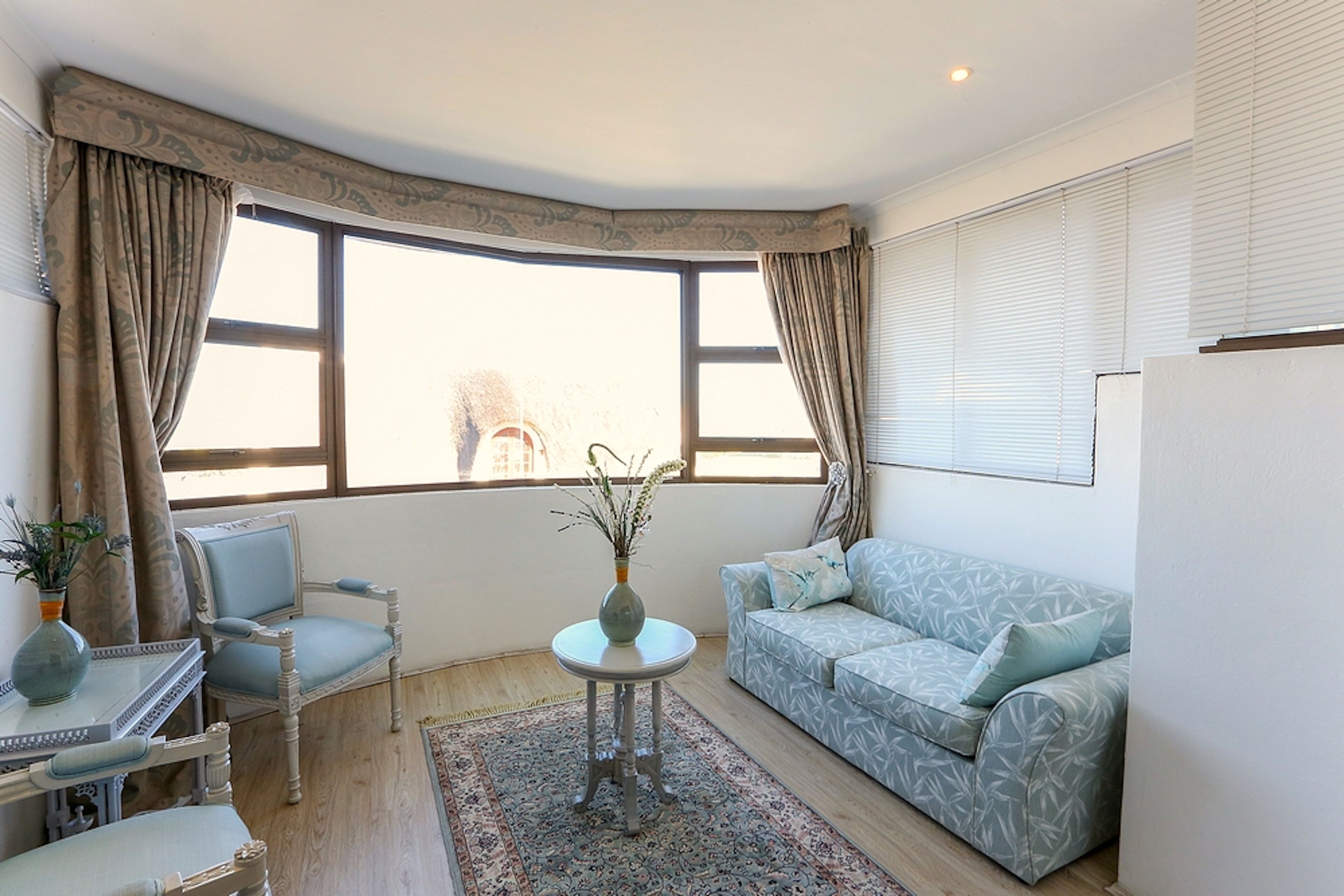A living room with a sofa, armchairs, a small table, and a window with curtains.