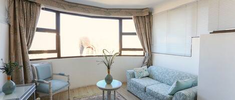 A living room with a sofa, armchairs, a small table, and a window with curtains.