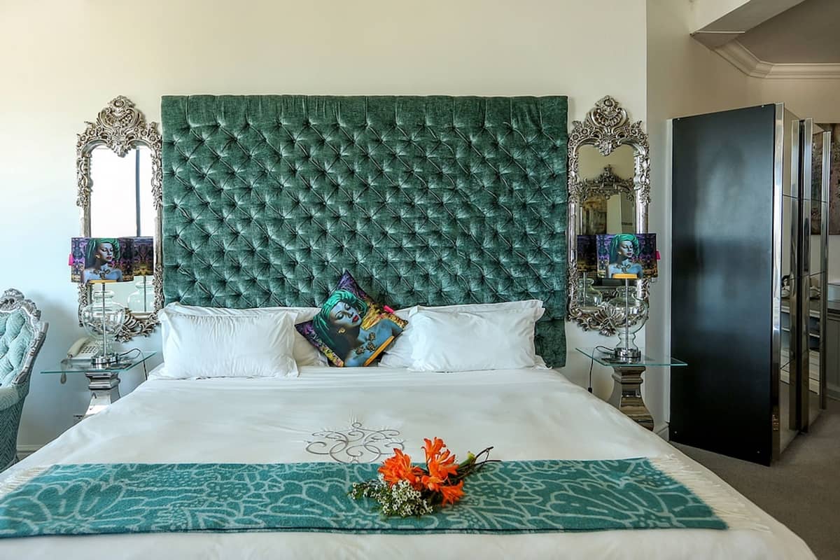 Une chambre d’hôtel avec un grand lit, une tête de lit recouverte d’un tissu vert, du linge de lit blanc et des coussins décoratifs.