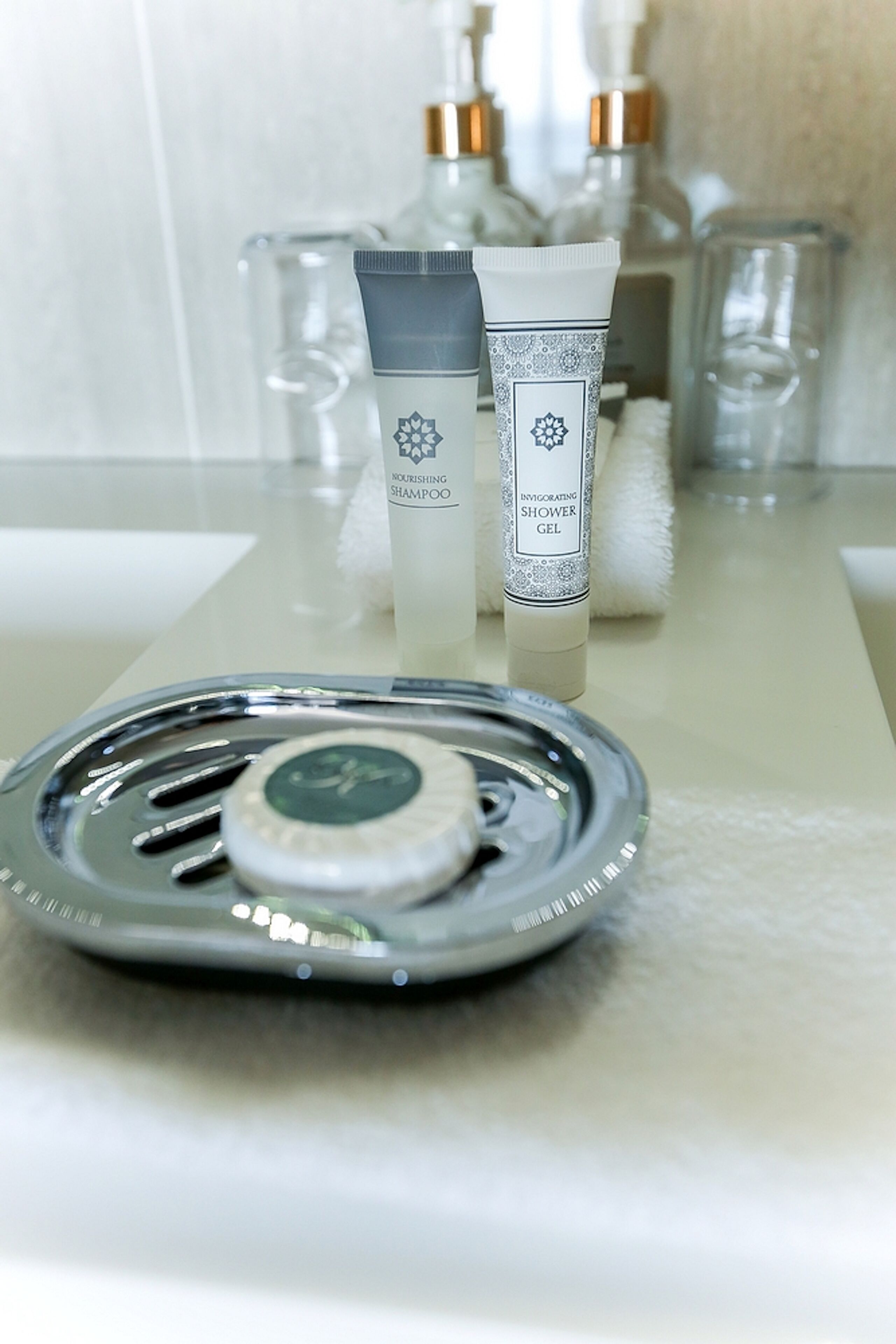 A bathroom counter with a hairdryer, two bottles of shampoo and shower gel, and a glass container.