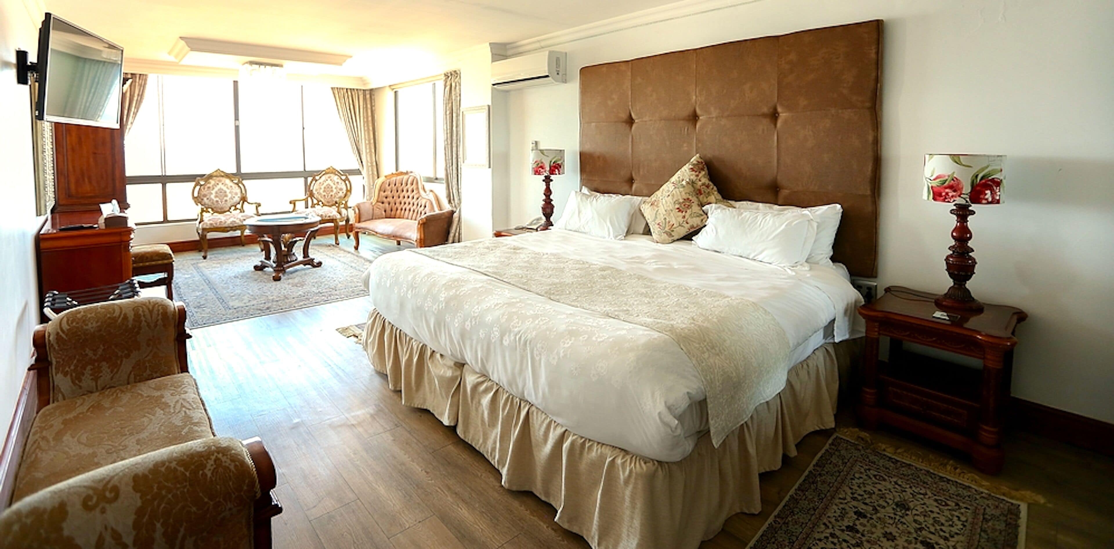 A spacious bedroom with a large bed, a sitting area with chairs, and a view of the outdoors.