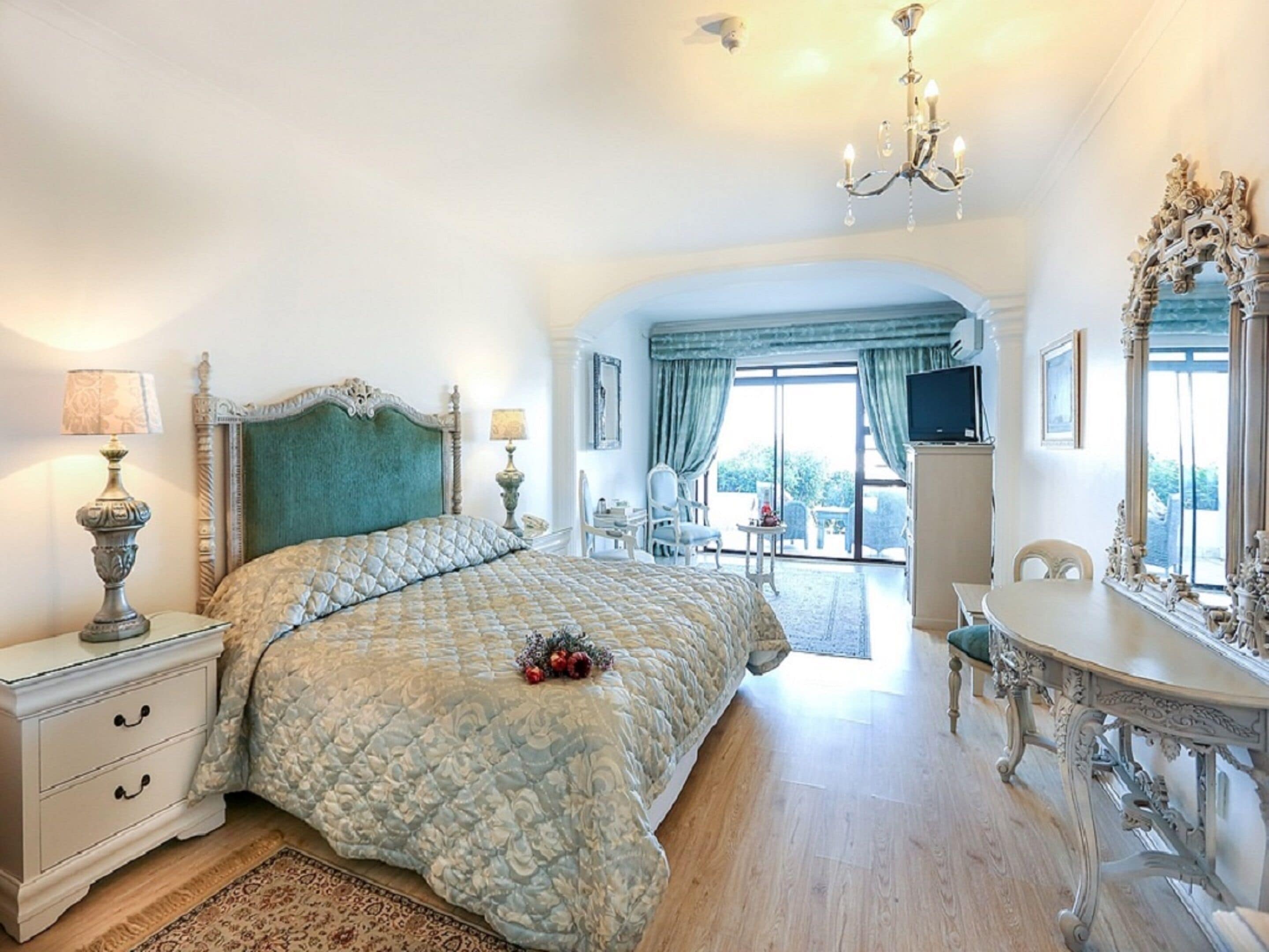 Ein geräumiges Schlafzimmer mit einem großen Bett, einer Kristallleuchter, einem Fernseher und einem Essbereich mit Tisch und Stühlen.