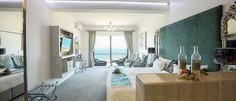 A modern hotel room with a bed, a desk, a bench, and a view of the ocean.