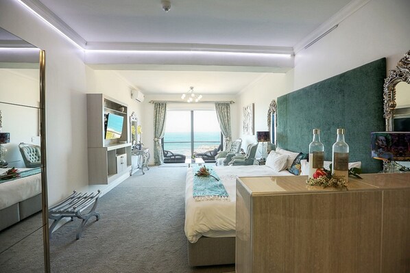 A modern hotel room with a bed, a desk, a bench, and a view of the ocean. - Misty Waves Boutique Hotel (Hermanus)