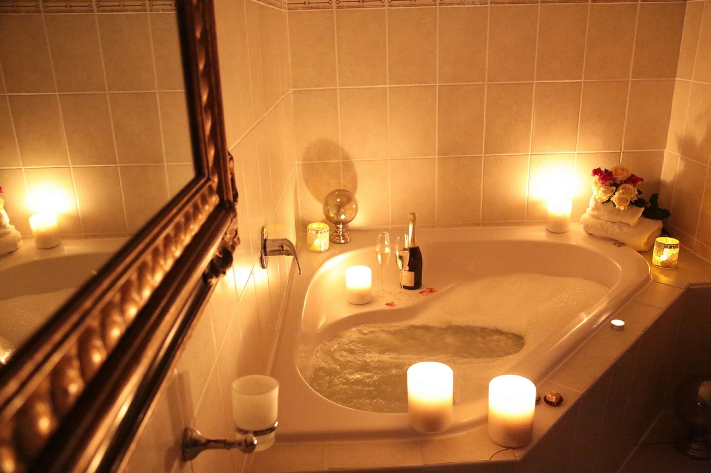 A bathroom with a bathtub, candles, and a mirror.