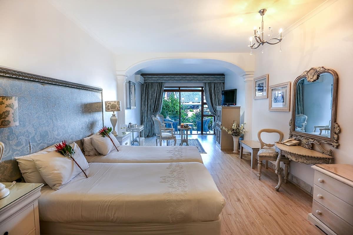 Une chambre spacieuse avec deux grands lits, une coiffeuse avec un miroir et une vue sur l’extérieur.