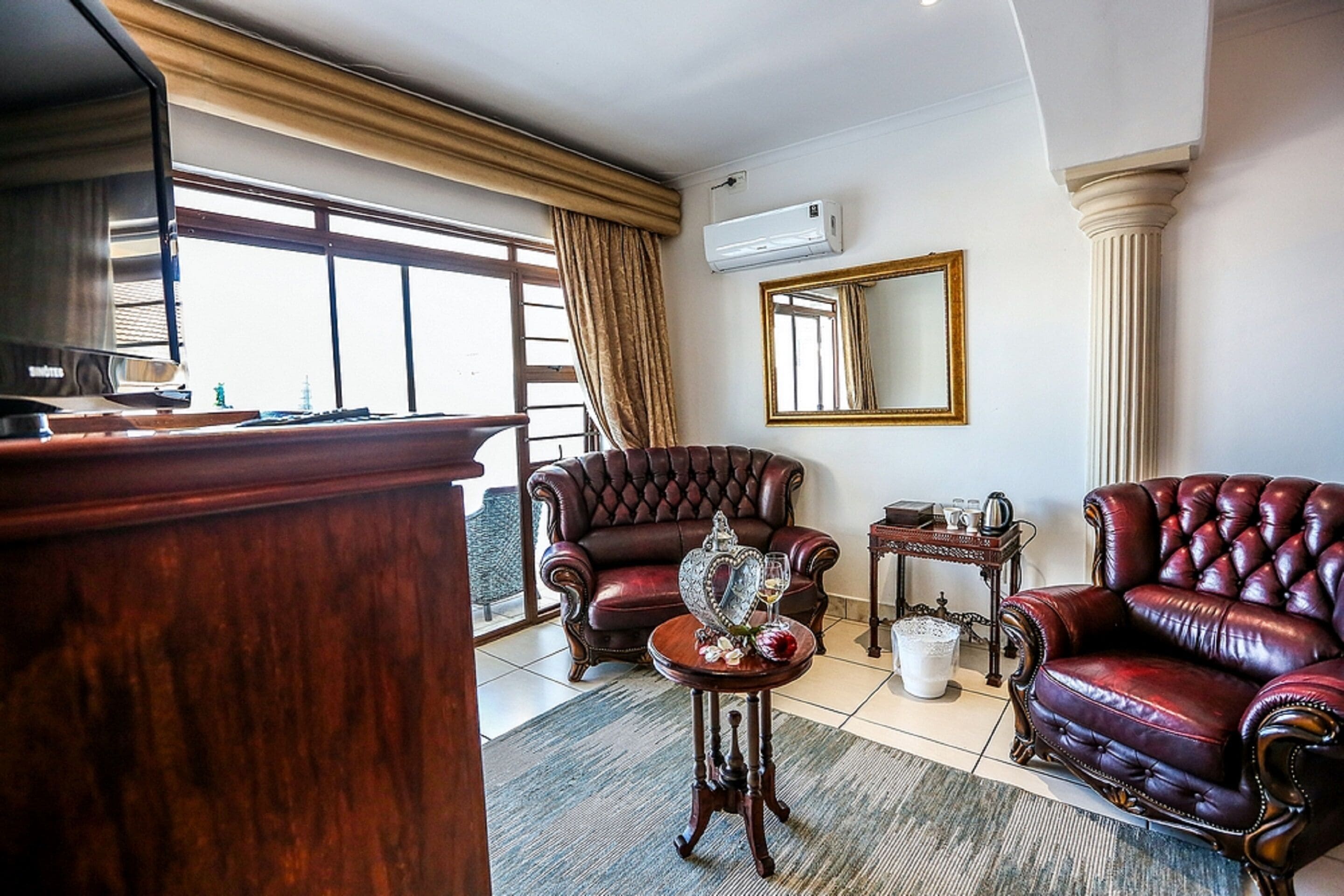 Una habitación con un ventanal grande, sillones de cuero, una mesita de madera y un espejo en la pared.