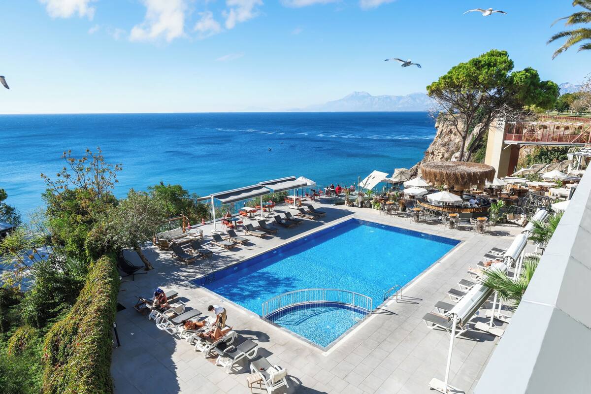 A pool area with lounge chairs, a swimming pool, and a view of the sea.