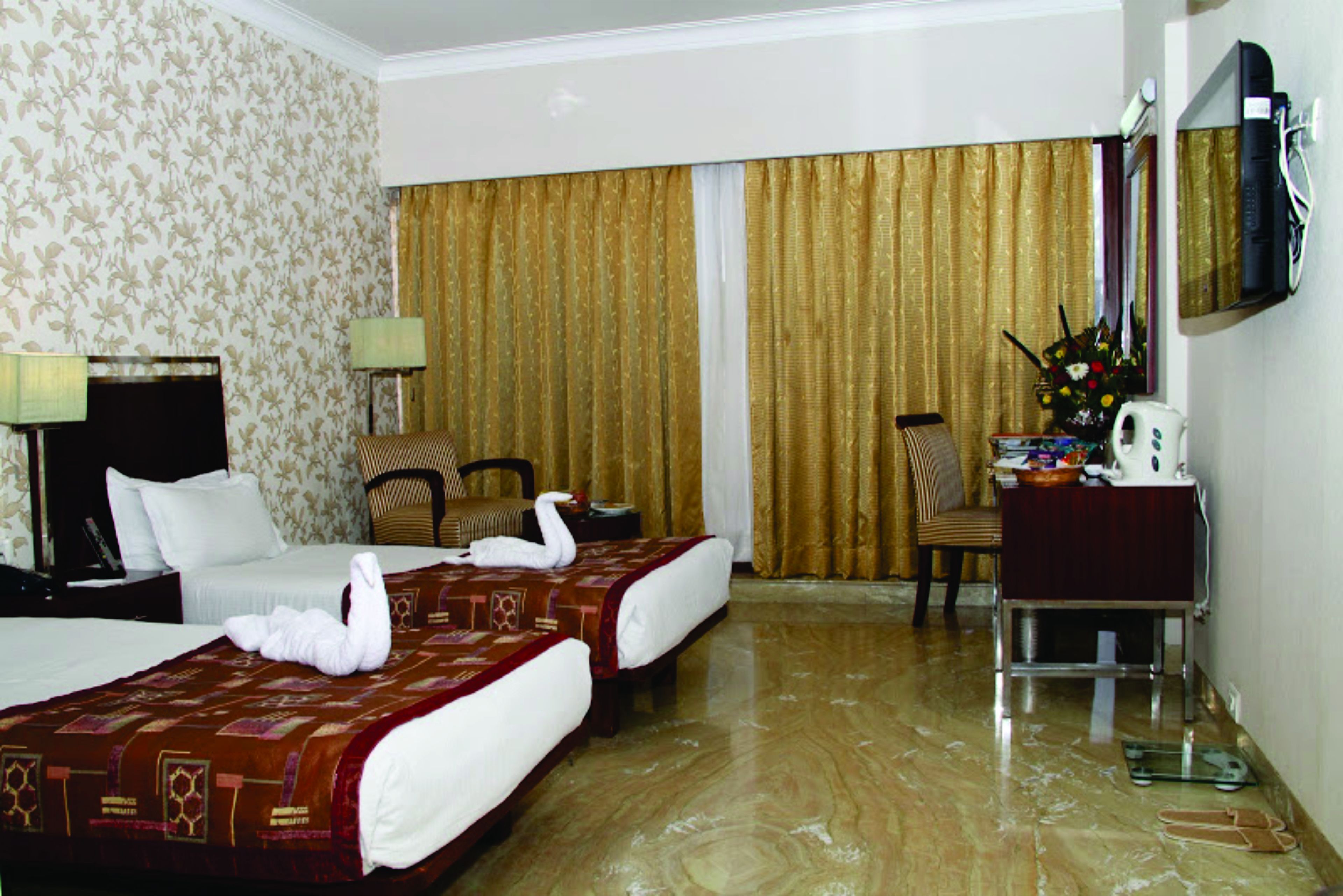 Quarto de hotel com duas camas, uma escrivaninha com cadeira, televisão e uma janela grande com cortinas.