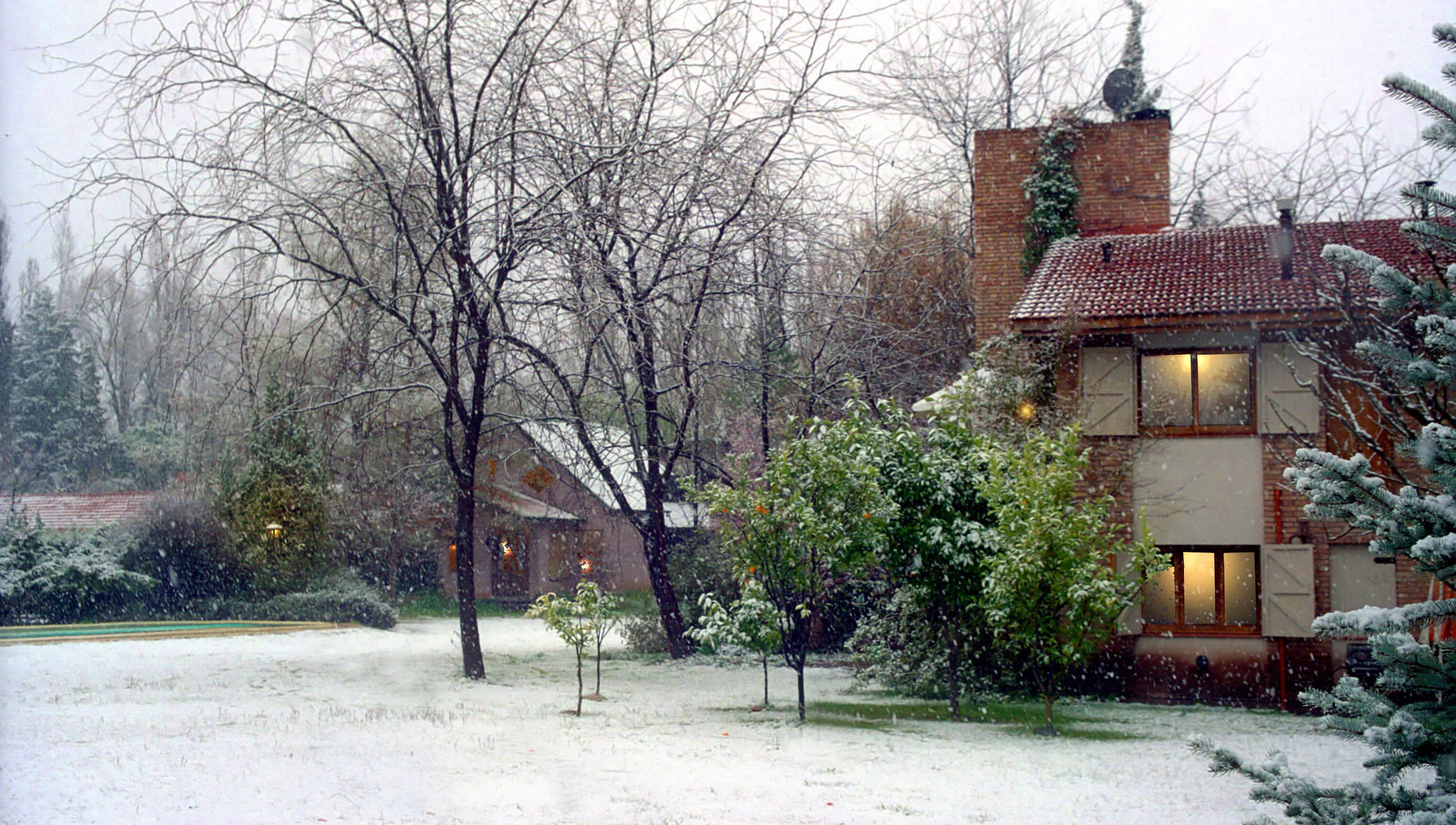 A snow-covered landscape with a house featuring a brick facade and a tiled roof.