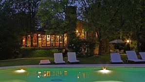 A poolside area with lounge chairs and a building with illuminated windows. - Casa Glebinias Hotel Jardin (Chacras de Coria)
