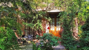 A rustic garden with a wooden bench and a table, surrounded by lush greenery and a stone pathway. - Casa Glebinias Hotel Jardin (Chacras de Coria)