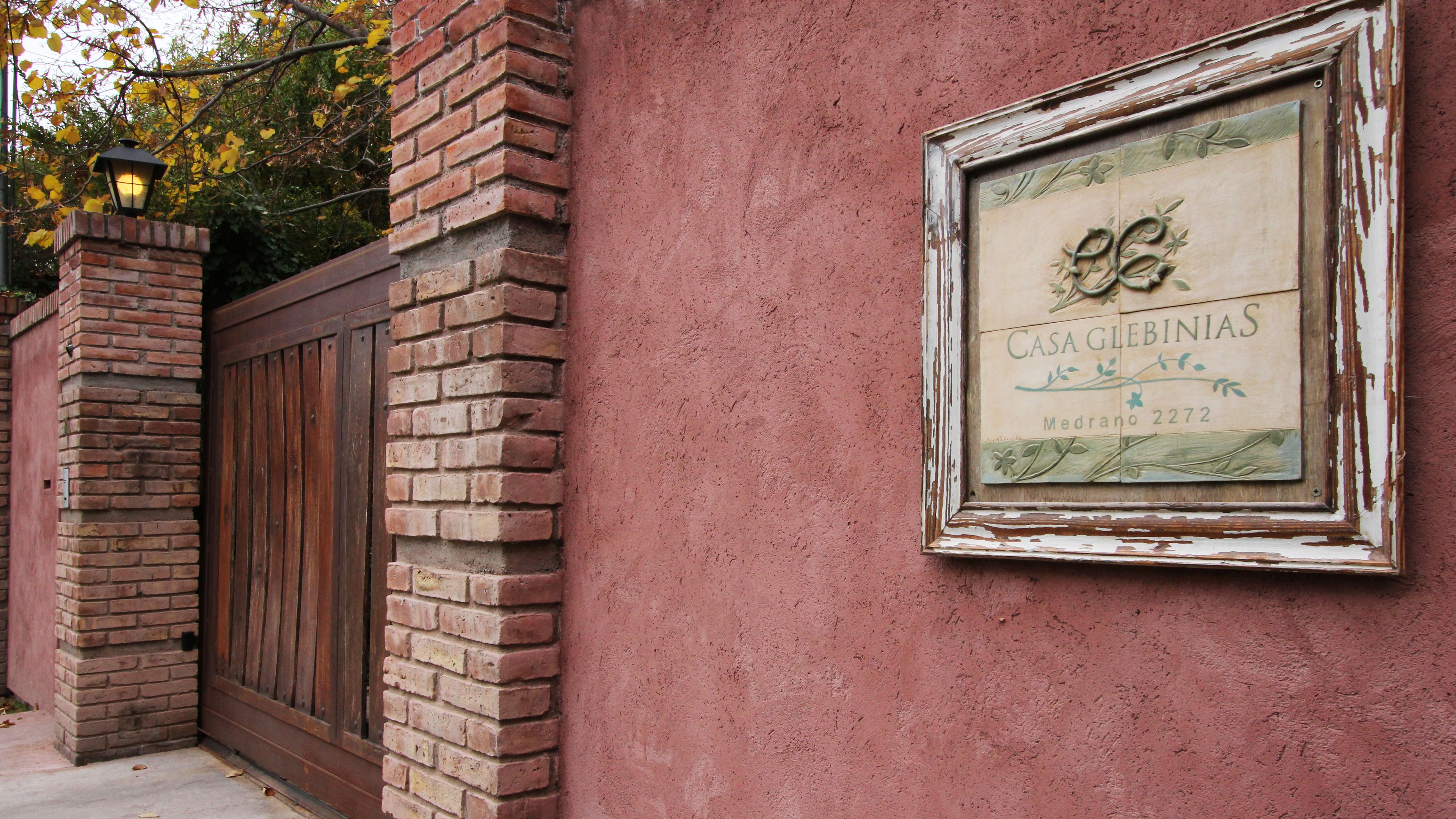 Paredão de tijolos com uma placa desgastada que diz 'CASA GLEBINIAS Medrano 2722'.