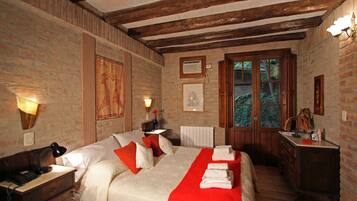 A bedroom with a large bed, wooden beams, a dresser, and a window with a view of greenery.