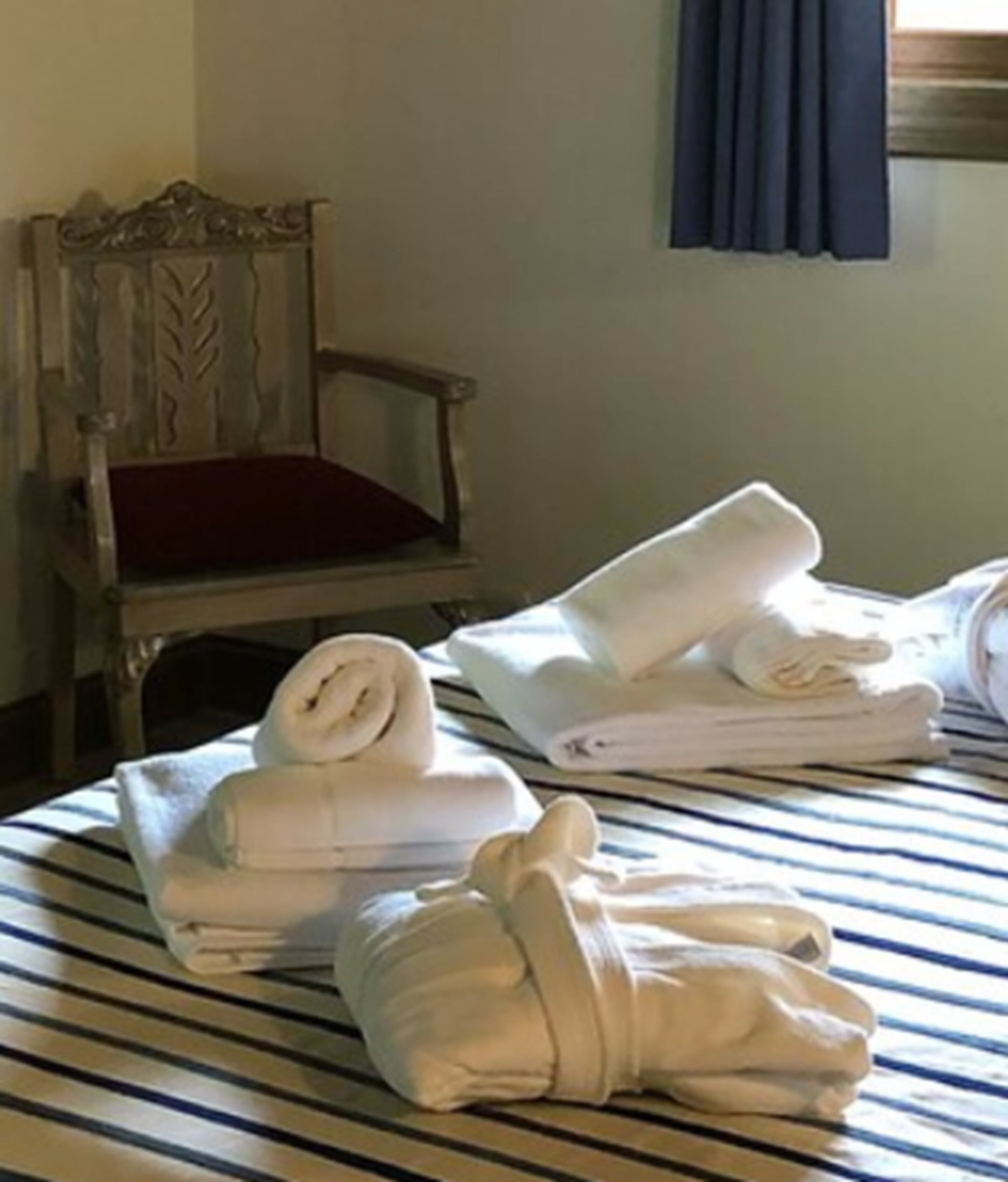 A bed with striped bedding, a wooden chair with a red cushion, and neatly folded towels.