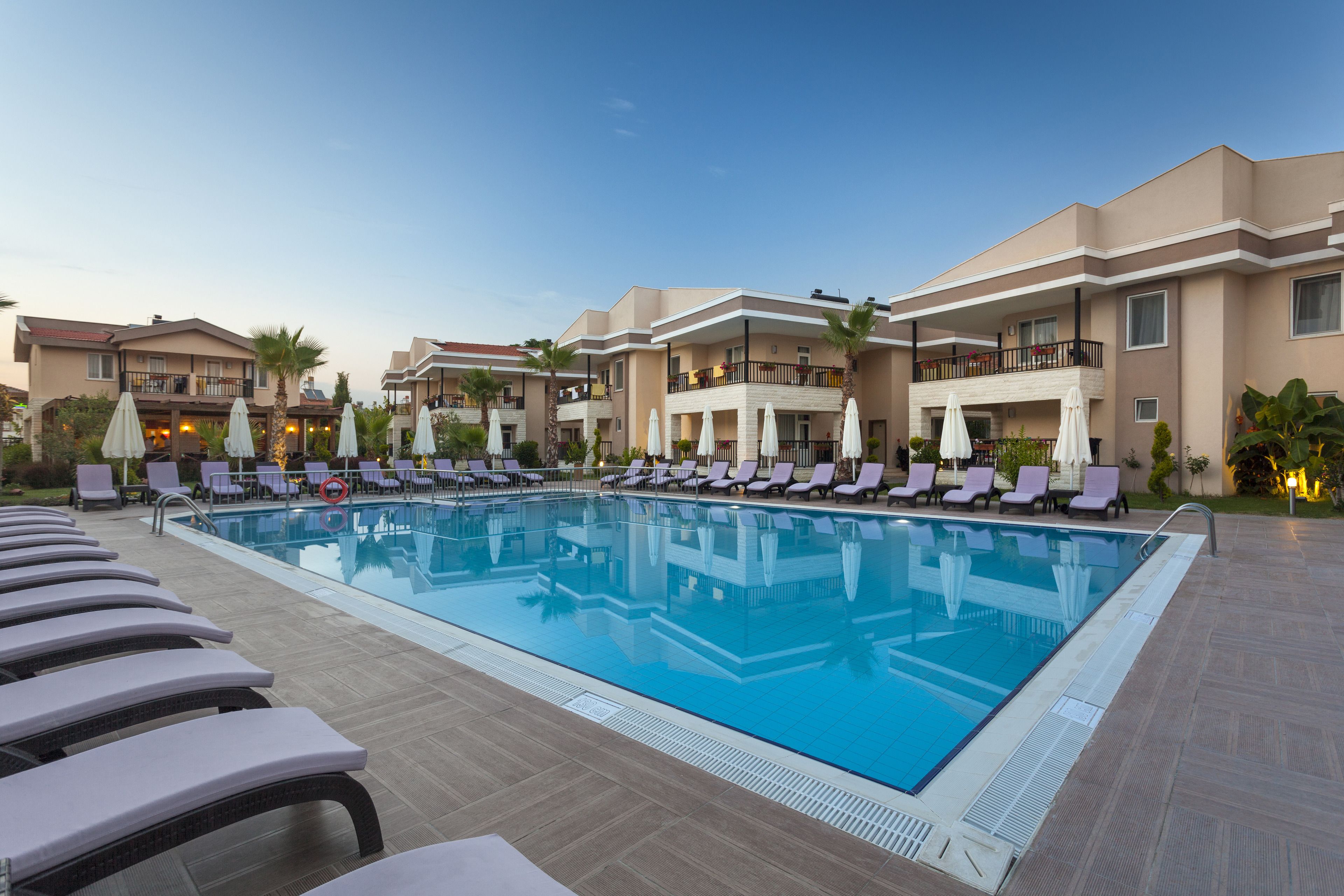A swimming pool with lounge chairs and umbrellas, surrounded by multi-story buildings with balconies.