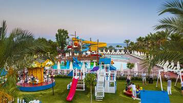 Relax and play in a vibrant water park surrounded by lush greenery and palm trees, featuring a swimming pool and multiple seating areas.