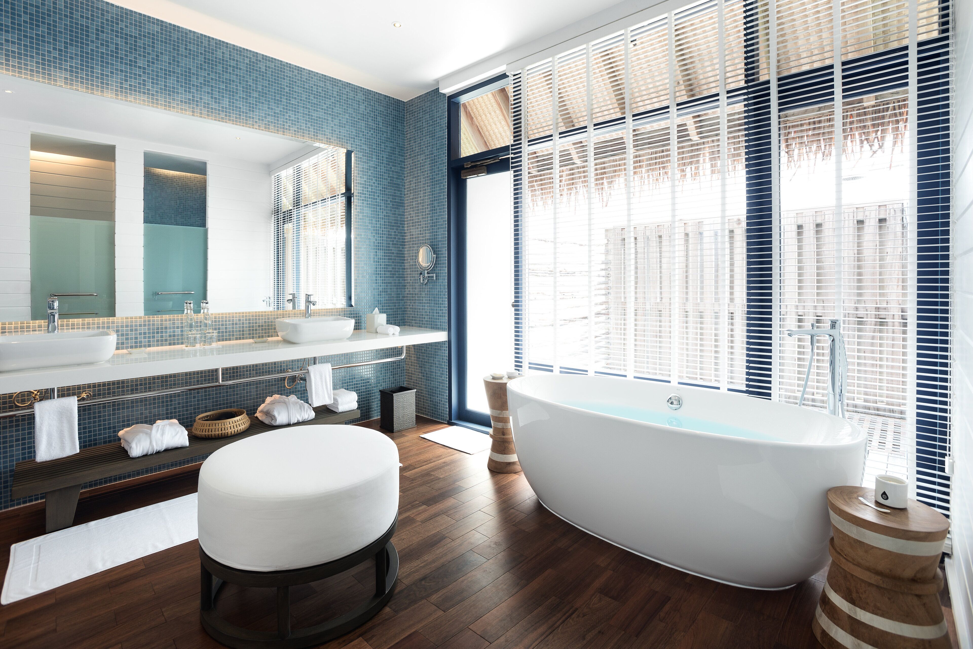 A modern bathroom with a freestanding bathtub, a large mirror, and a blue-tiled wall.