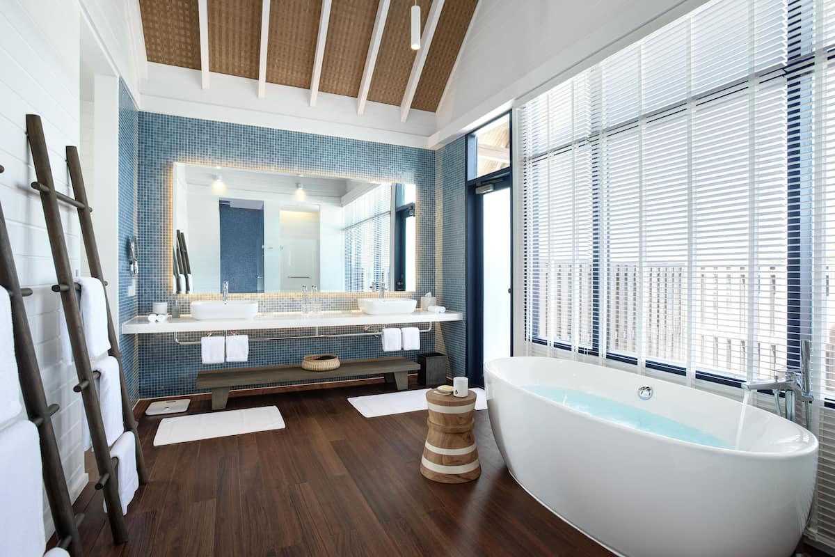 Ein modernes Badezimmer mit einer großen Badewanne, einem Waschtisch mit Spiegel und einem Fenster mit Jalousien.
