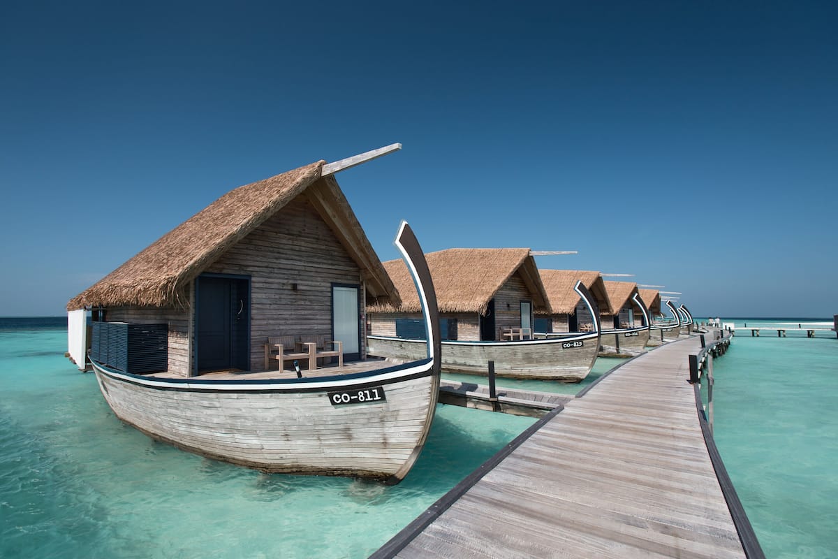 Bungalows auf Stelzen über türkisfarbenem Wasser, mit Reetdächern und Holzsteigen.