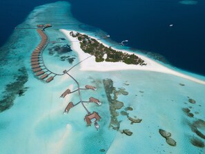 An aerial view of a resort with overwater bungalows connected by walkways, a sandy beach, and clear turquoise waters. - COMO Cocoa Island (Makunufushi)