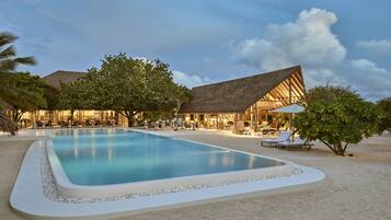 A resort with a swimming pool, lounge chairs, and a thatched-roof building.