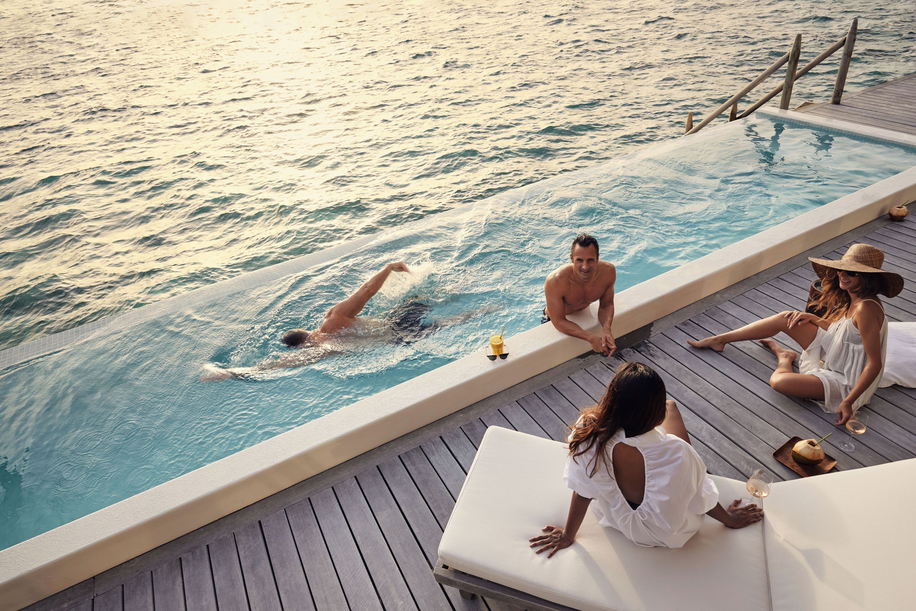 Un área junto a la piscina con un jacuzzi, sillas de descanso y una terraza de madera.