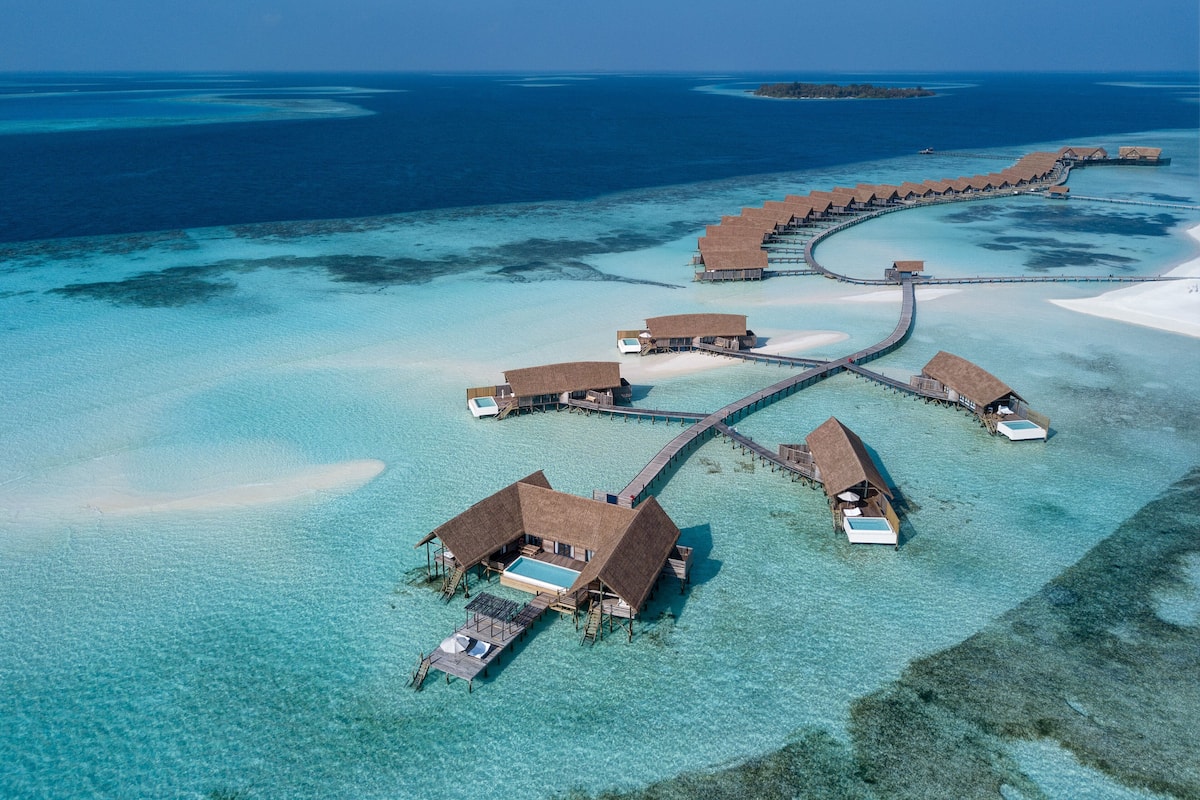 Ein Resort mit Bungalows über dem Wasser, verbunden durch einen langen Steg.