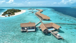 An overwater bungalows with thatched roofs, connected by a wooden walkway, in a clear turquoise sea.