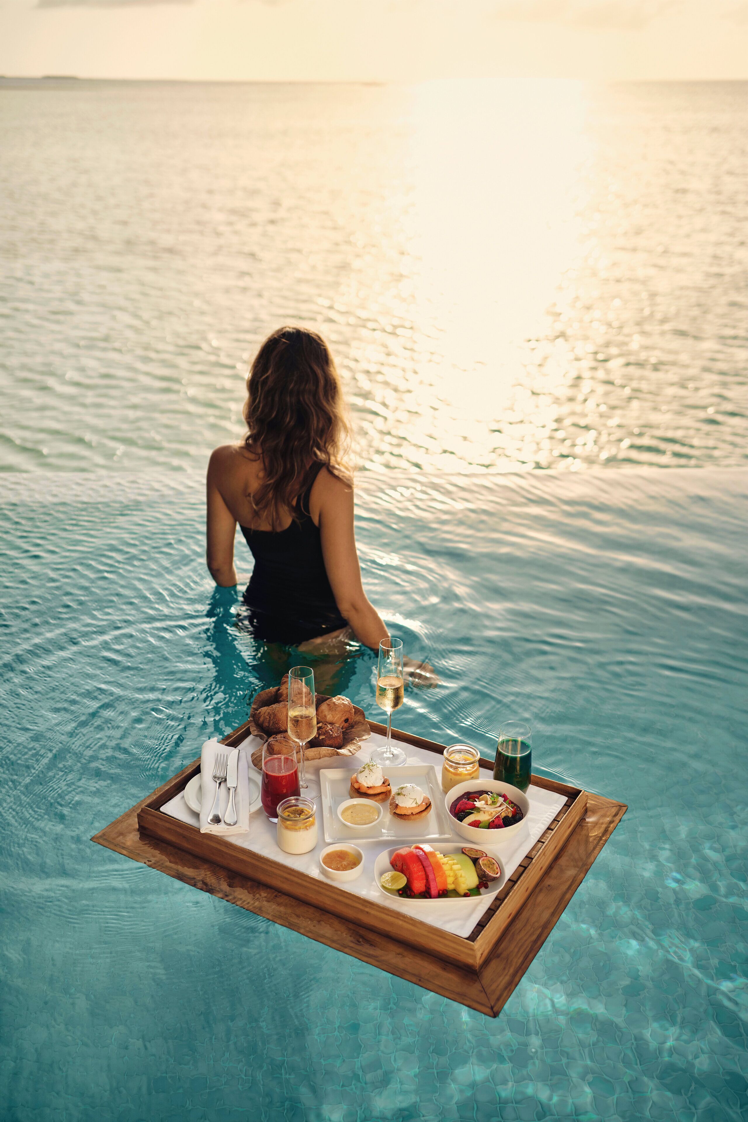 Una persona en una piscina con una bandeja de comida y bebidas.