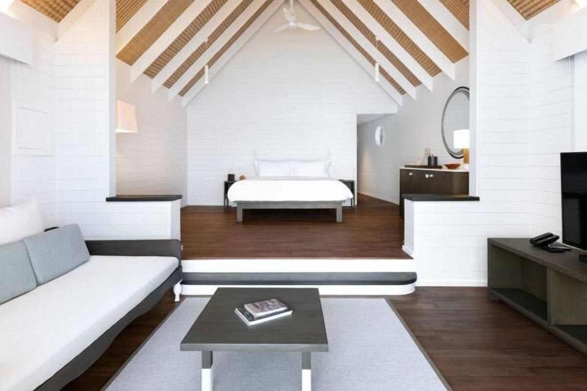 Ein modernes Loft-Schlafzimmer mit schrägem Dach, einem Bett, einer Couch, einem Couchtisch und einem Fernseher.