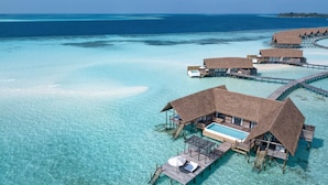 An overwater bungalow with a pool, wooden deck, and thatched roof.