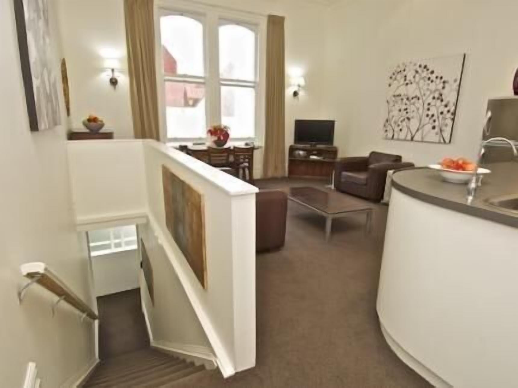 Una sala de estar moderna con un sofá, una mesa de centro y un televisor. Una escalera conduce a un nivel superior.