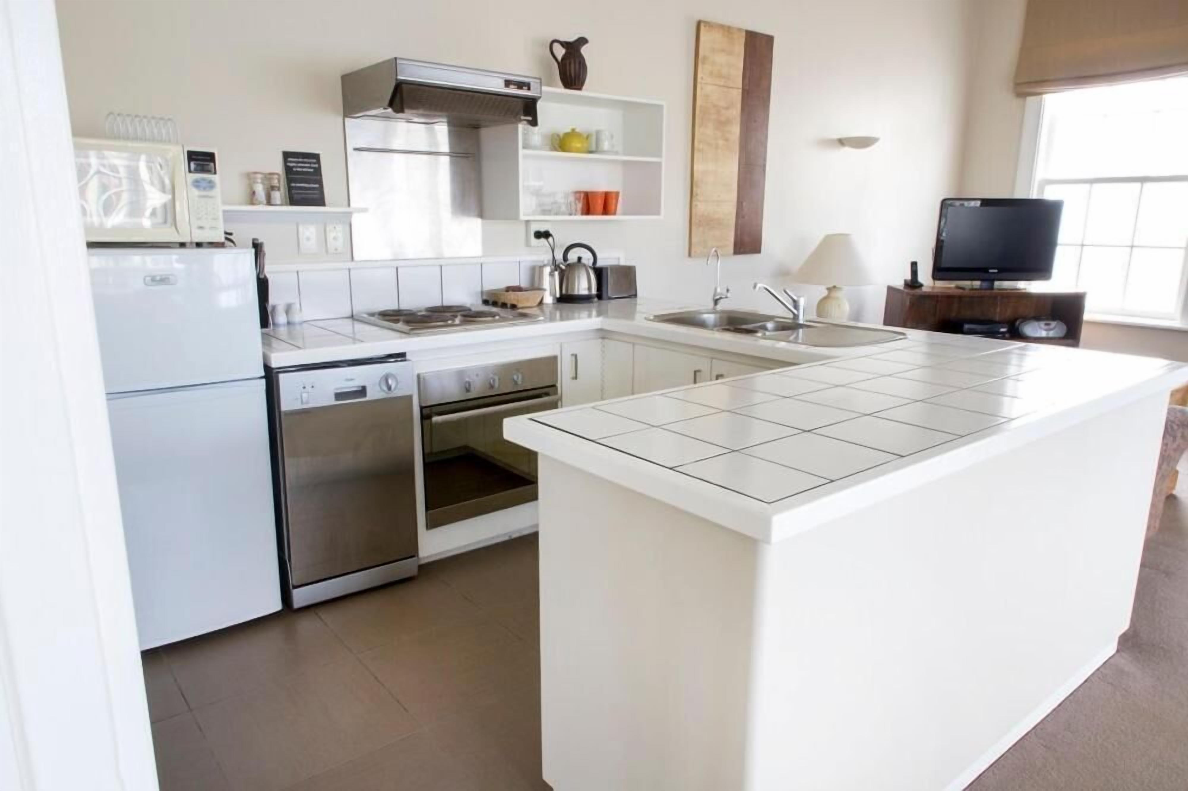 Uma cozinha moderna com armários brancos, forno embutido, micro-ondas e uma ilha grande com bancada revestida em azulejo.