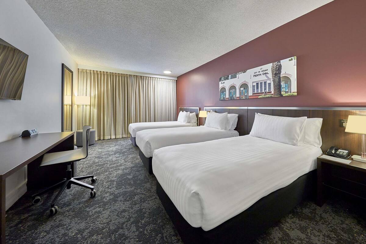 A hotel room with two beds, a desk, a chair, a lamp, and a painting on the wall.