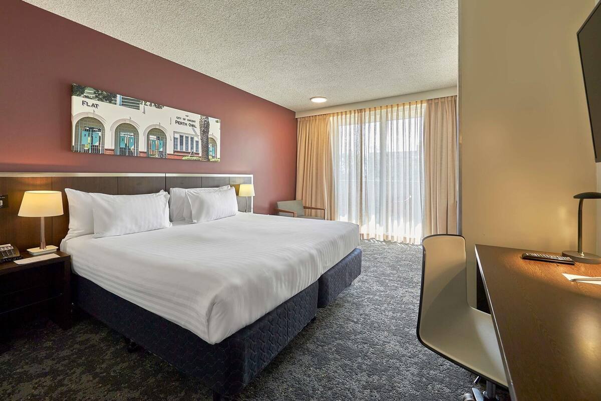 Een hotelkamer met een groot bed, een bureau, een stoel, een lamp en een schilderij aan de muur.